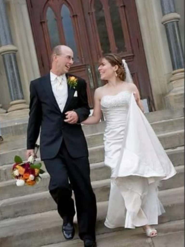 A woman in a wedding dress and man in a tuxedo after a wedding on church steps smiling.