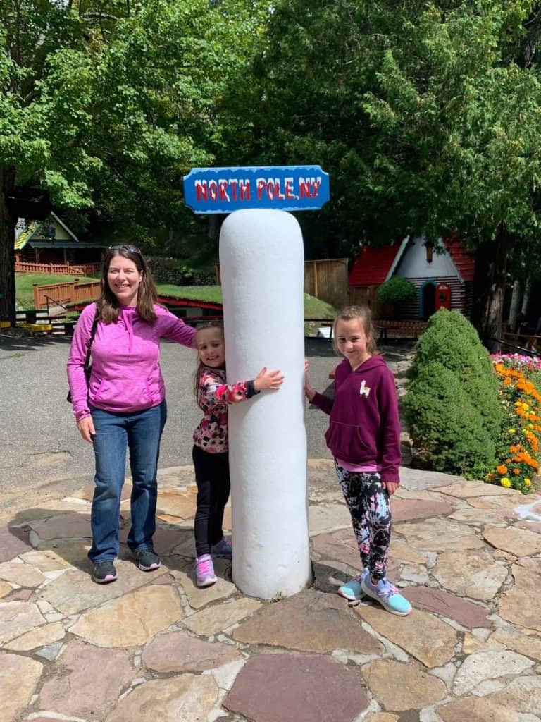 A mom and two girls smiling next to North Pole, NY icy post tourist attraction in New York.