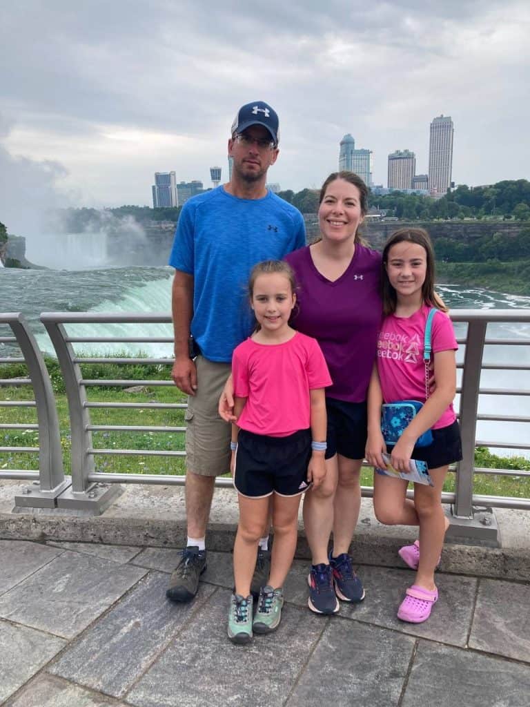 A family of 4 in shorts on a bridge overlooking Niagara Falls, NY waterfalls.