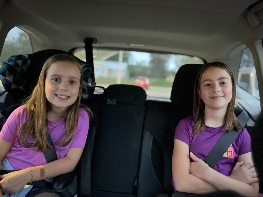 Two girls in purple in a car backseat on a day trip.