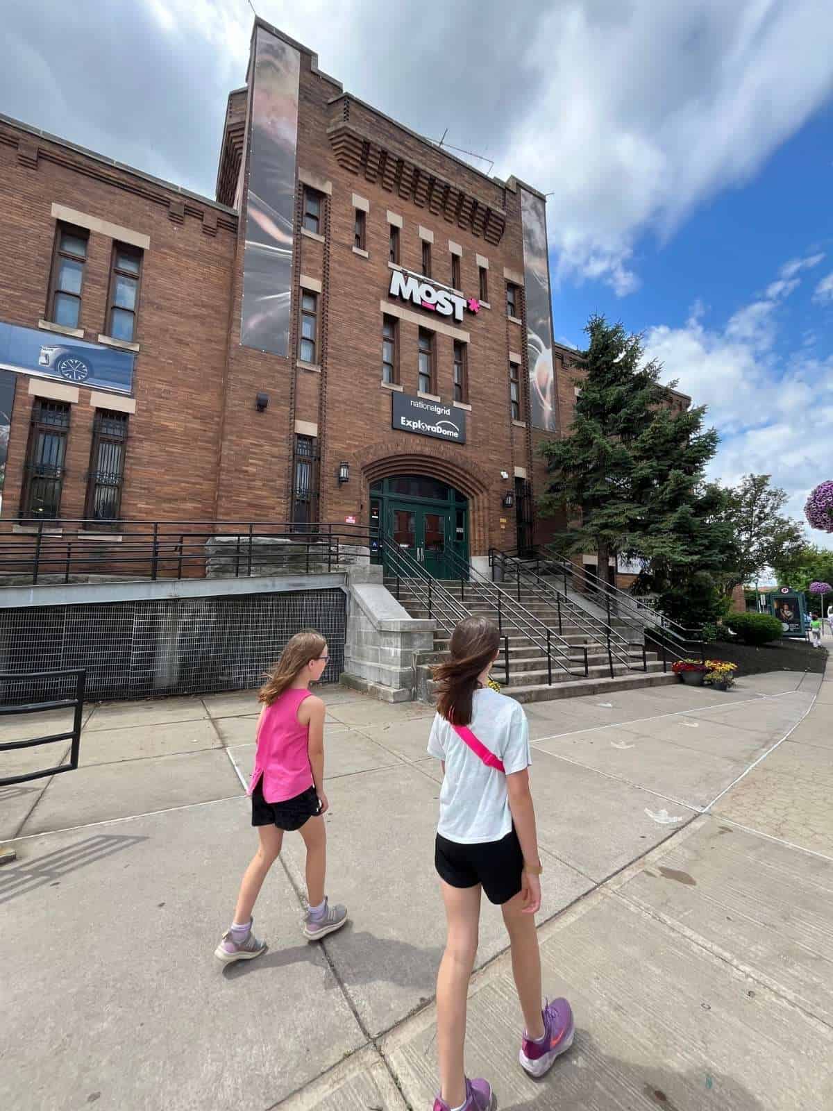 Two girls walk toward a brick science building with a MOST sign on it.