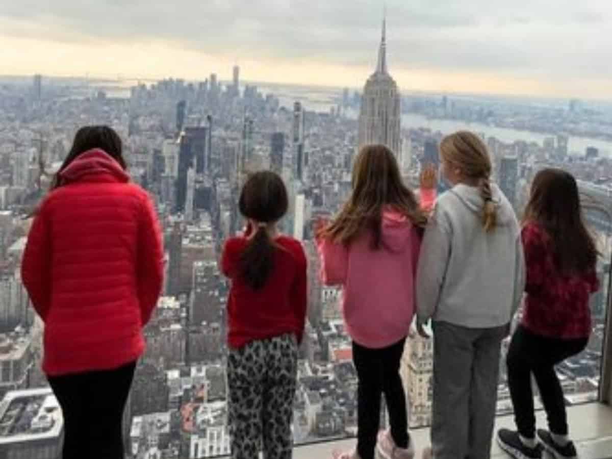Five kids in colorful jackets and shirts facing a view overlooking NYC skyline and buildings.