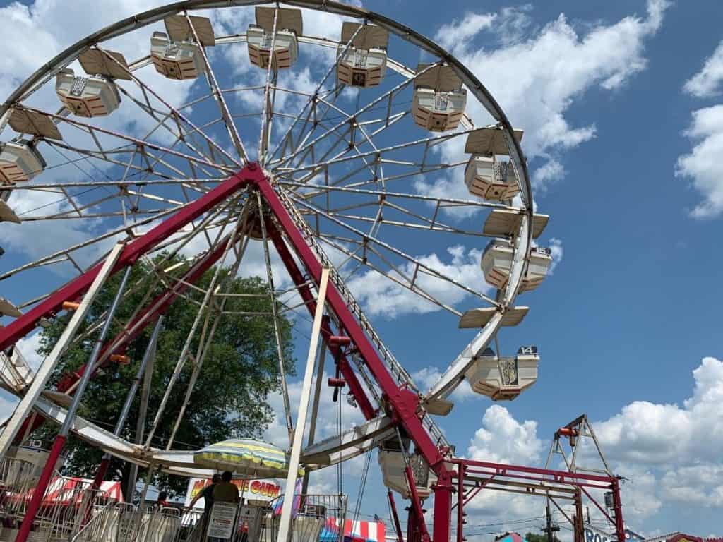Looking up at a Ferris wheel on day with blue sky and white fluffy clouds.