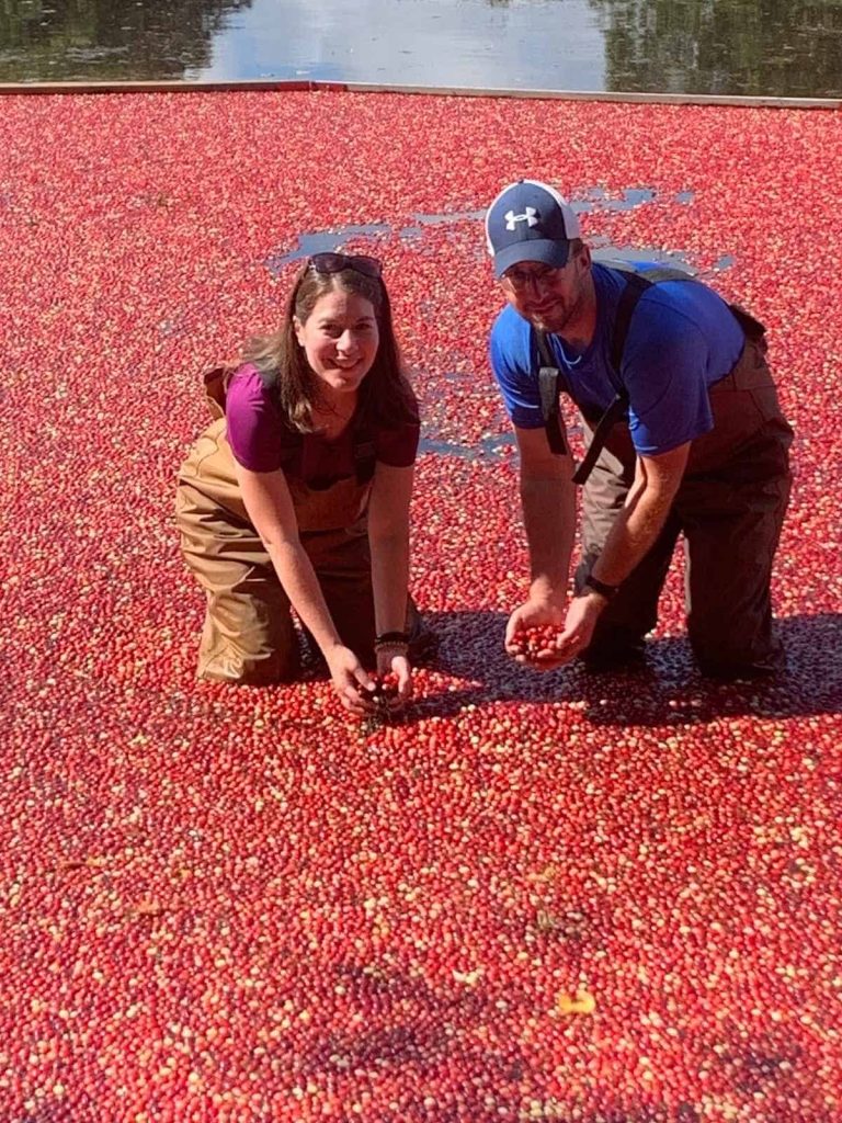 A woman and man on a Family Cranberry Bog Tour in waders surrounded by floating red cranberries.