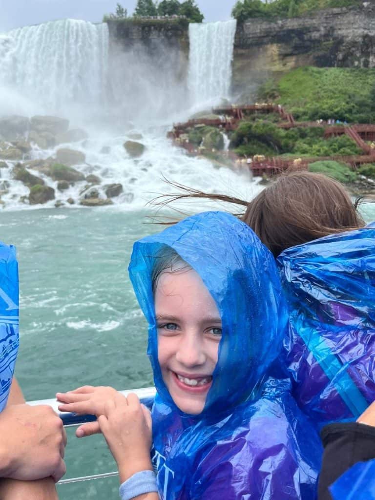 Girl in a blue poncho, riding the family-friendly attraction the Maid of the Mist boat at Niagara Falls, NY, with waterfalls in the background.