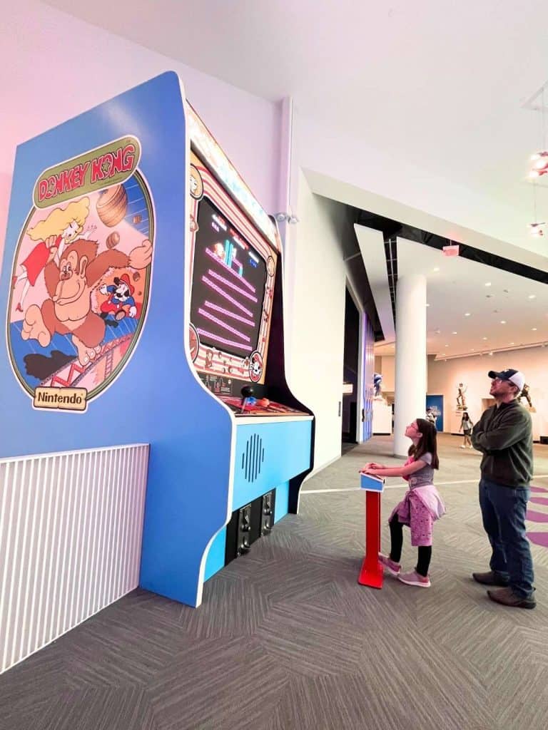 A girl and a dad looking up at and playing a 12-foot Donkey Kong arcade video game.