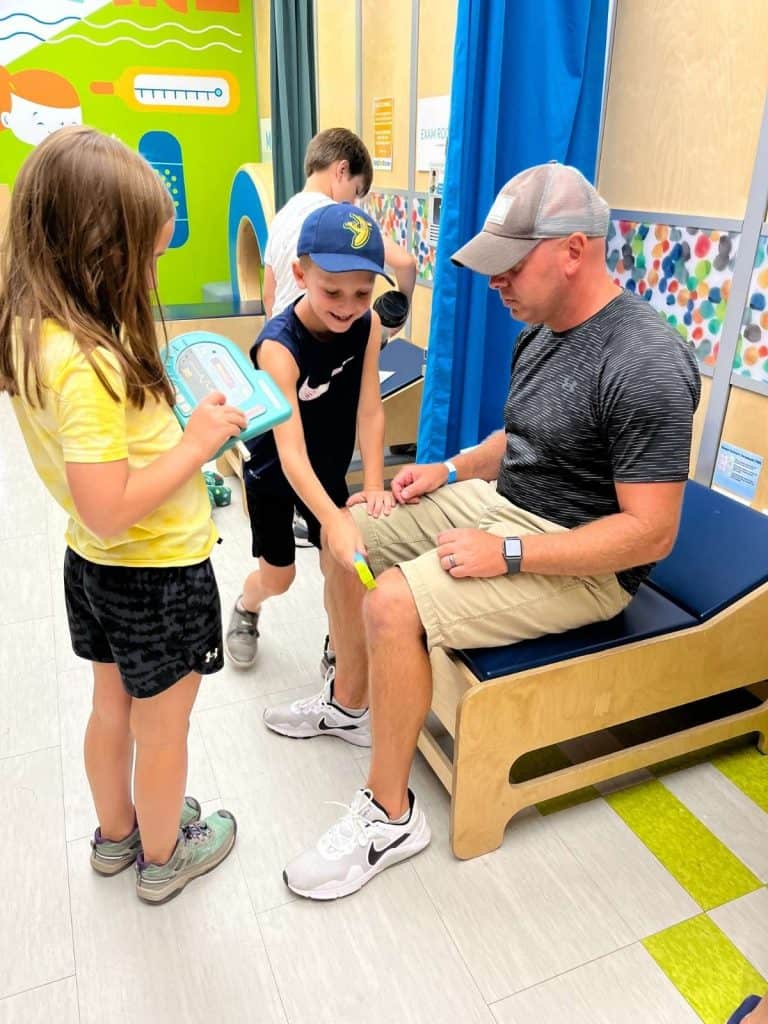 Two children and a dad playing in a brightly colored hospital attraction at the family friendly Explore & More Children's Museum in Upstate Buffalo, NY.