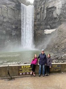 A woman and two girls in front of Taughannock Falls State Park large waterfall attraction surrounded by rock walls.