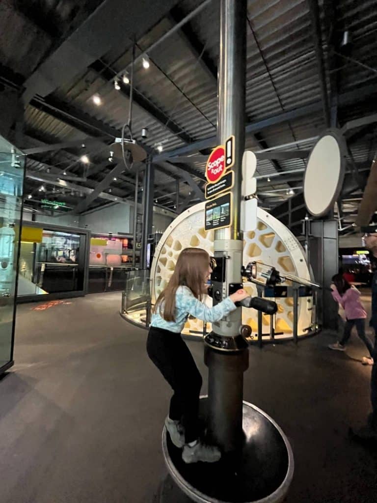 A child interacts with a large periscope exhibit in the Innovation Center with exhibits behind her.