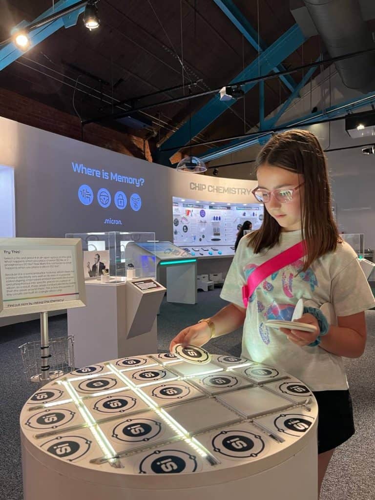 A girl interacting with a glowing exhibit of chemistry symbols with computers in the background at a Syracuse, NY science museum.