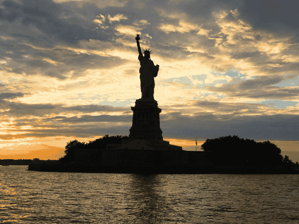 The Statue of Liberty is backlit by the sun setting.