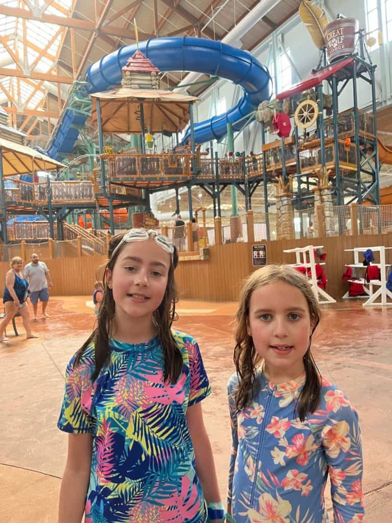 Two girls stand in front of a giant indoor water slide and park area.