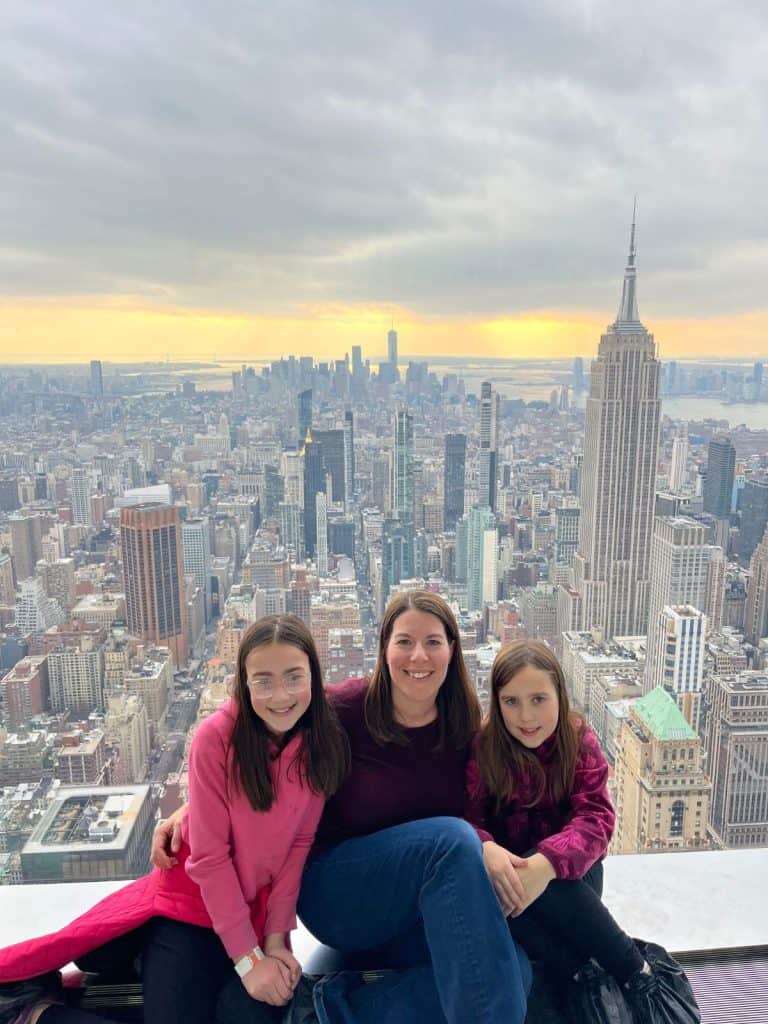 A family posing at an observation deck with the Empire State Building and NYC skyline behind them.