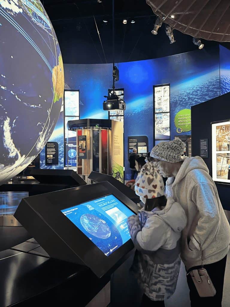 A family exploring a space exhibit at a computer station in a dimly lit room of the Air and Space Museum.