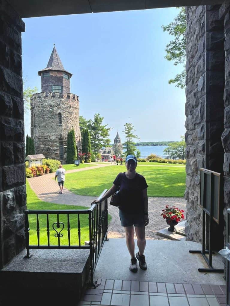 Boldt Castle views along the St. Lawrence on a Thousand Islands family itinerary A woman standing under a stone arched doorway with a view of the a castle building, grass, and the river in the background.