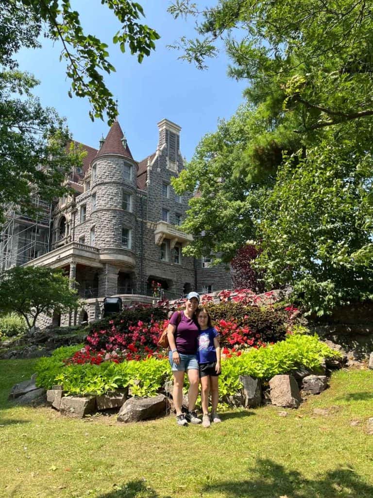 This is a family photo with a mom and daughter in front of Boldt Castle. A woman and girl posing in front of a large colorful flower garden with a castle in the background.