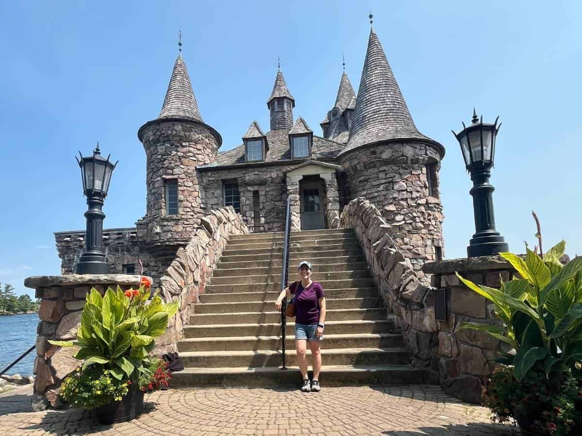 A woman standing in front of a castle's front steps with a blue sky.