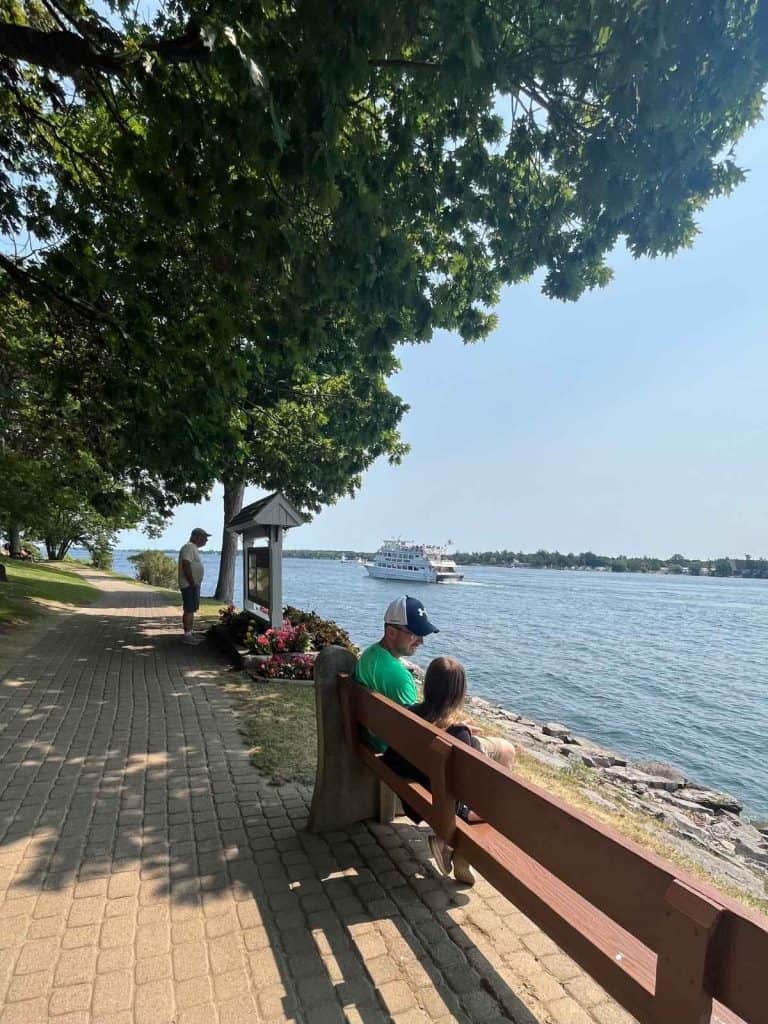 Relaxing riverside stop during a Thousand Islands family day trip Dad and daughter sitting on a bench watching boats on the St. Lawrence River