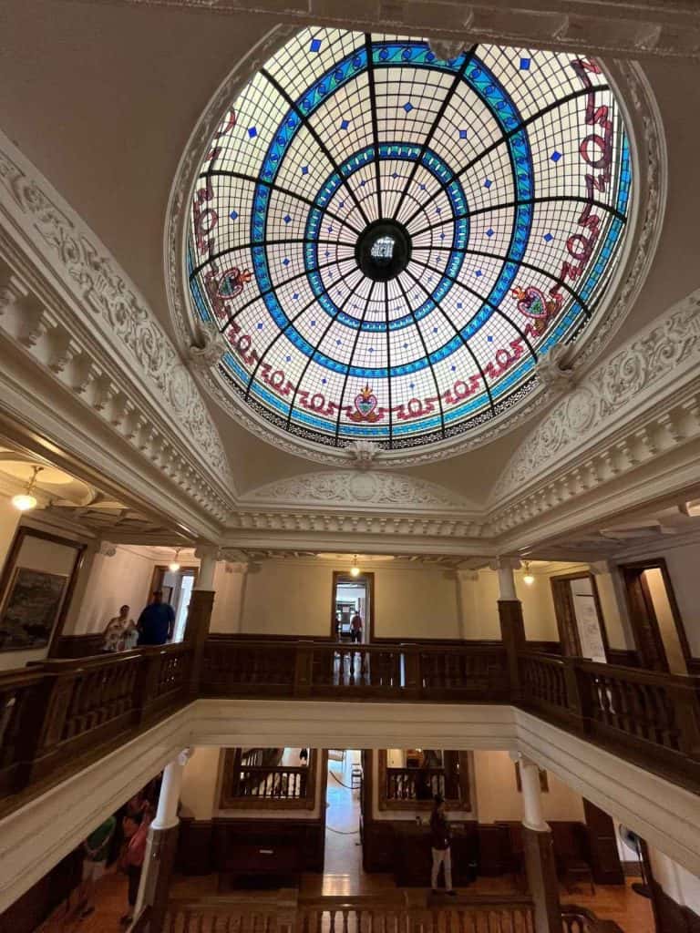 Historic stained glass inside Boldt Castle on Heart Island. Colorful round stained glass window at the top of a vaulted ceiling with hallways and railings leading to rooms off to the side.
