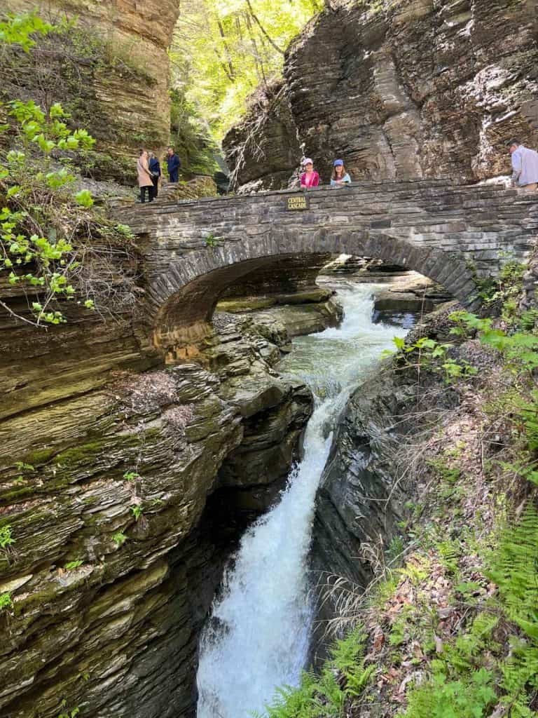 On a day trip to Watkins Glen with kids, showing how they love the stone bridge overlooking waterfalls. Two girls on a stone bridge above a Watkins Glen cavern with waterfall moving below them.