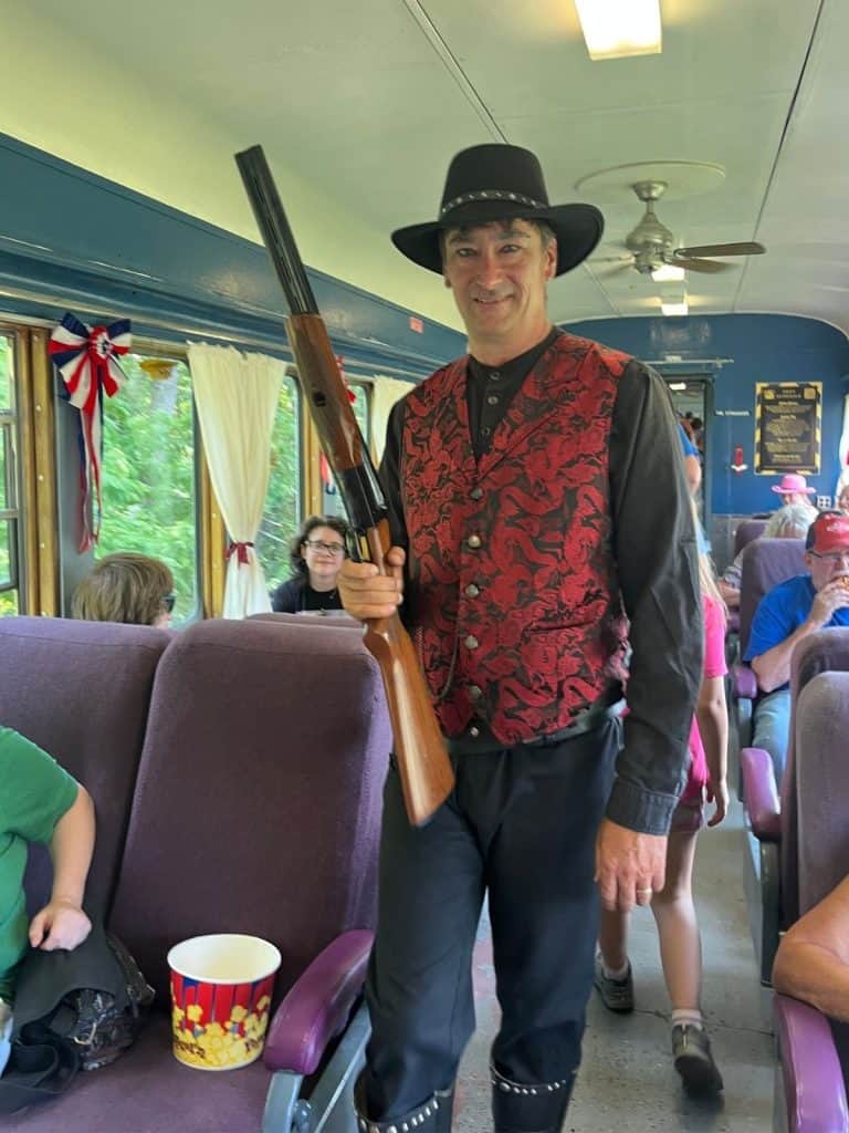 A smiling train robbery actor with a gun and period outfit stalks up the aisle to greet families.