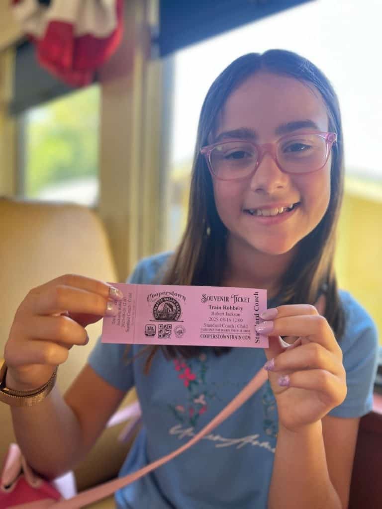 A smiling girl shows off her souvenir ticket to the Cooperstown train ride.