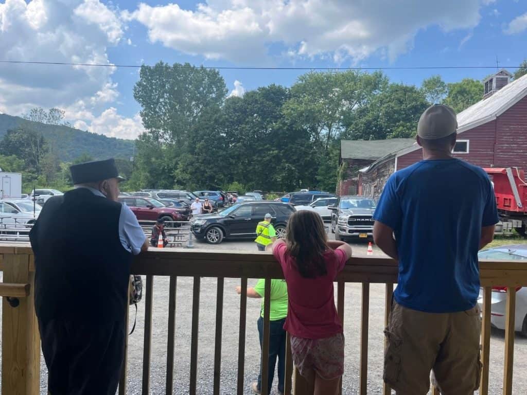 A father, daughter, and man in a conductor outfit look out at the parking lot and a dirt arena in front of the train station where the shootout will take place.