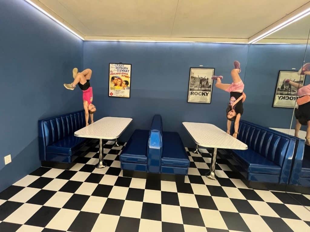 Two girls hanging upside down in a diner as part of the optical illusion at the Museum of Illusions Philadelphia.