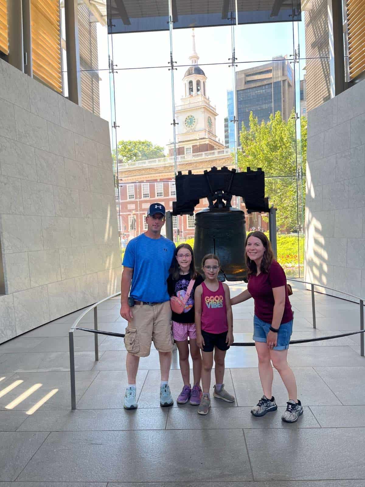 A family of 4 in front of the Philadelphia Liberty Bell with Independence Hall in the background.