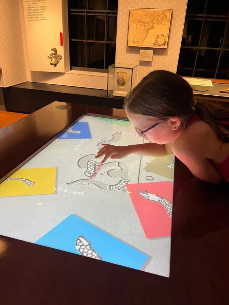 A girl piecing together a puzzle on an interactive computer screen in a dim museum room.