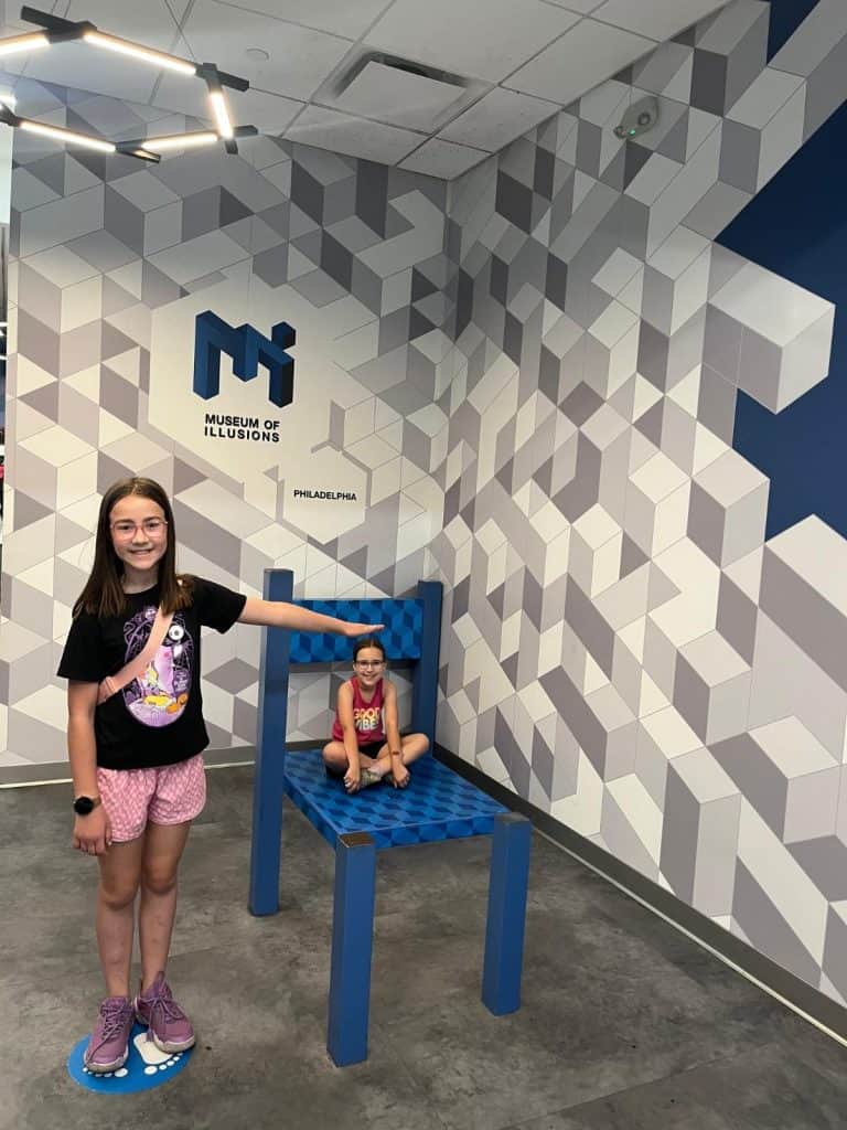 Two girls doing the giant chair optical illusion at the Museum of Illusions Philadelphia.