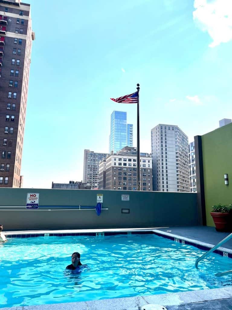 A girl swimming at the hotel pool on a rooftop with Philadelphia city buildings all around.
