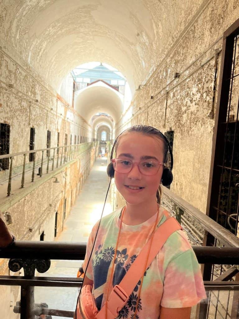Girl with audio tour headphones at a brightly lit cell block inside Eastern State Penitentiary in Philadelphia