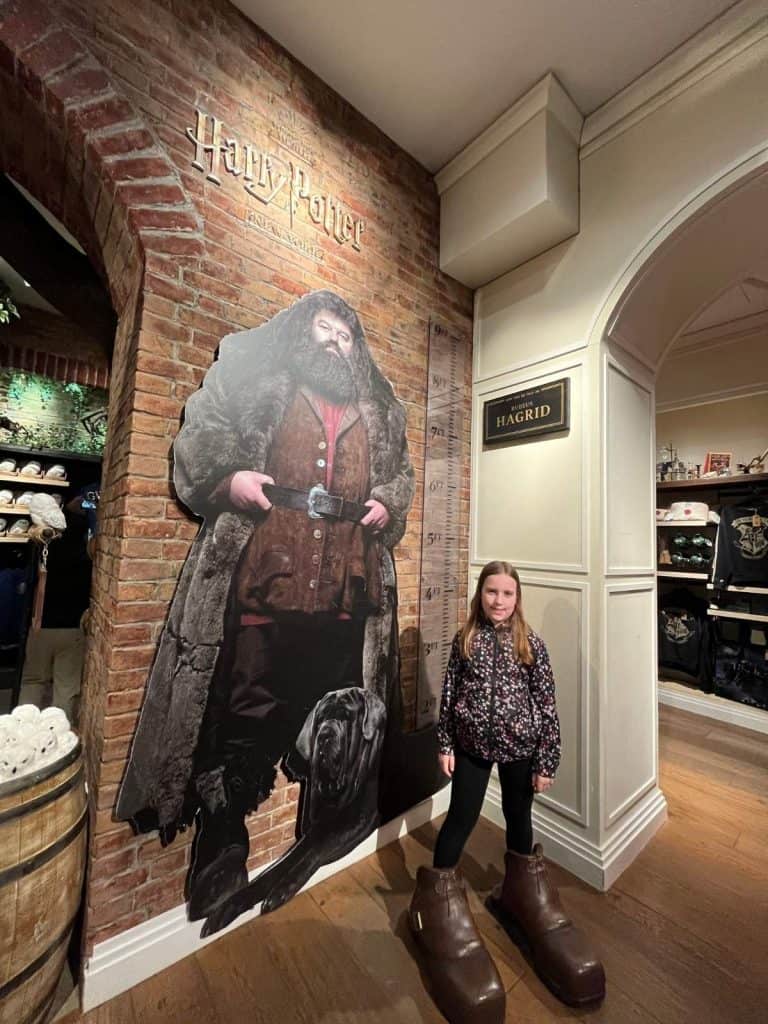 A girl stands next to a Harry Potter movie character named Hagrid's giant boots and 9 foot tall poster at the NYC Harry Potter Store.