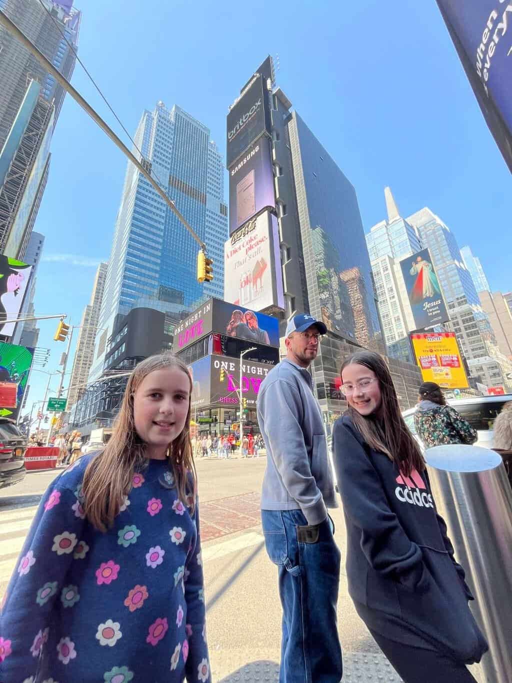 A family stands in Times Square with colorful billboards and tall buildings around them on their first trip to NYC.